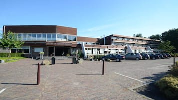 A hotel with a modern design, featuring a prominent entrance and a parking area with several cars.