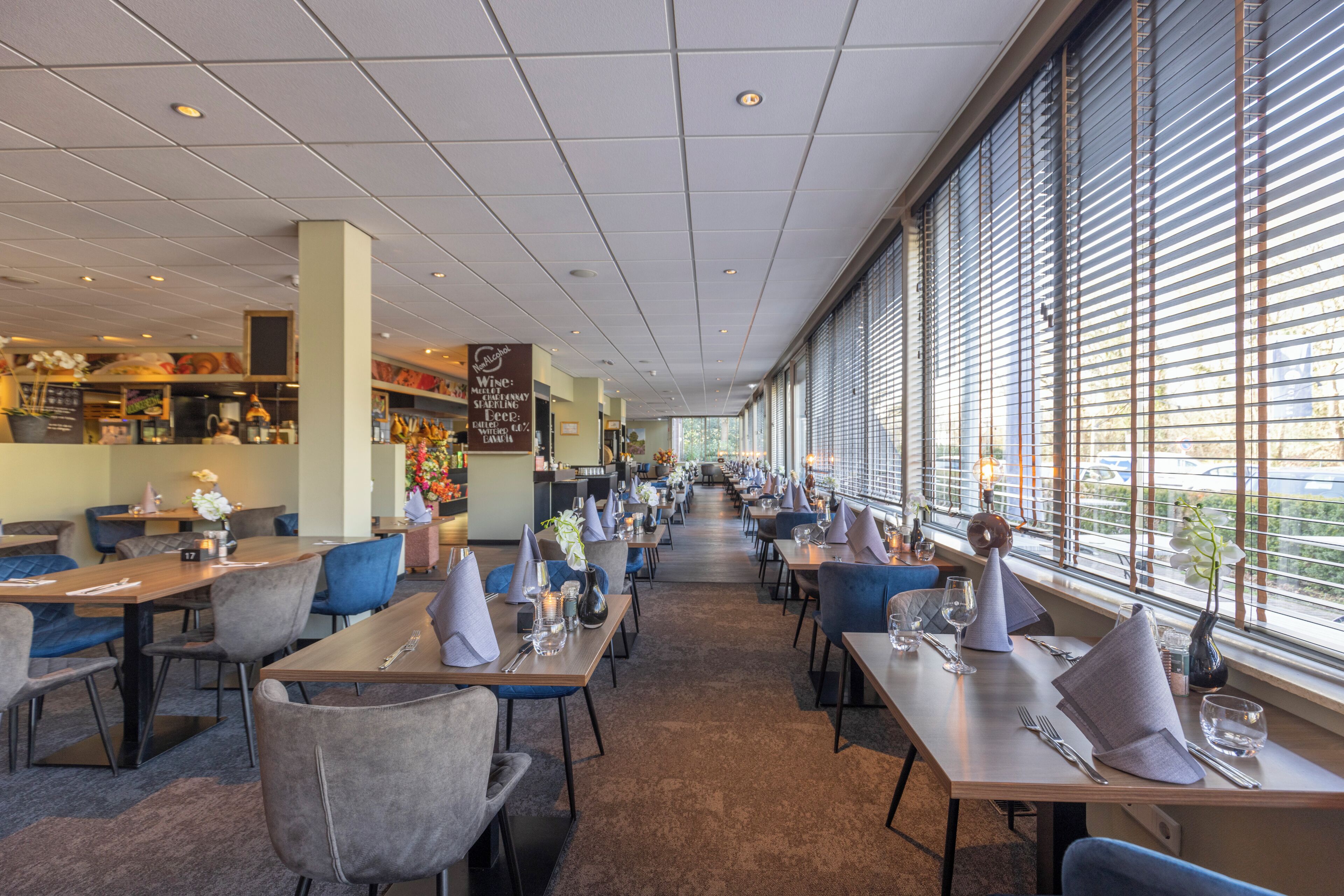 Un restaurant avec des tables et des chaises, un comptoir où est affiché le menu, et de grandes fenêtres.
