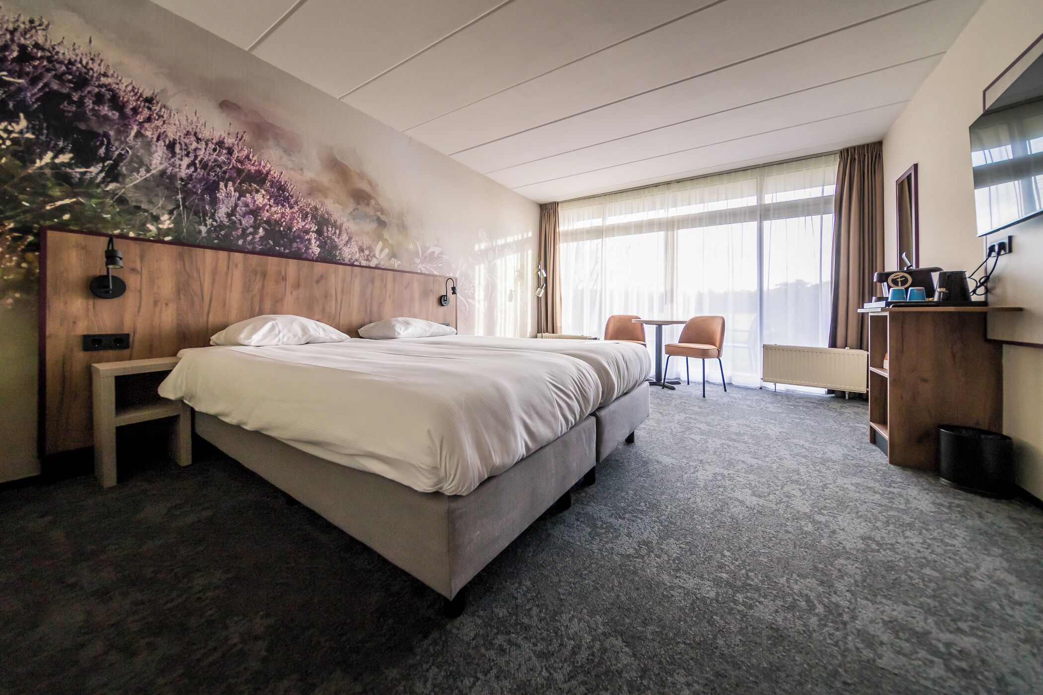 A hotel room with a bed, a desk, a chair, and a large window.