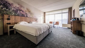 A hotel room with a bed, a desk, a chair, and a large window.