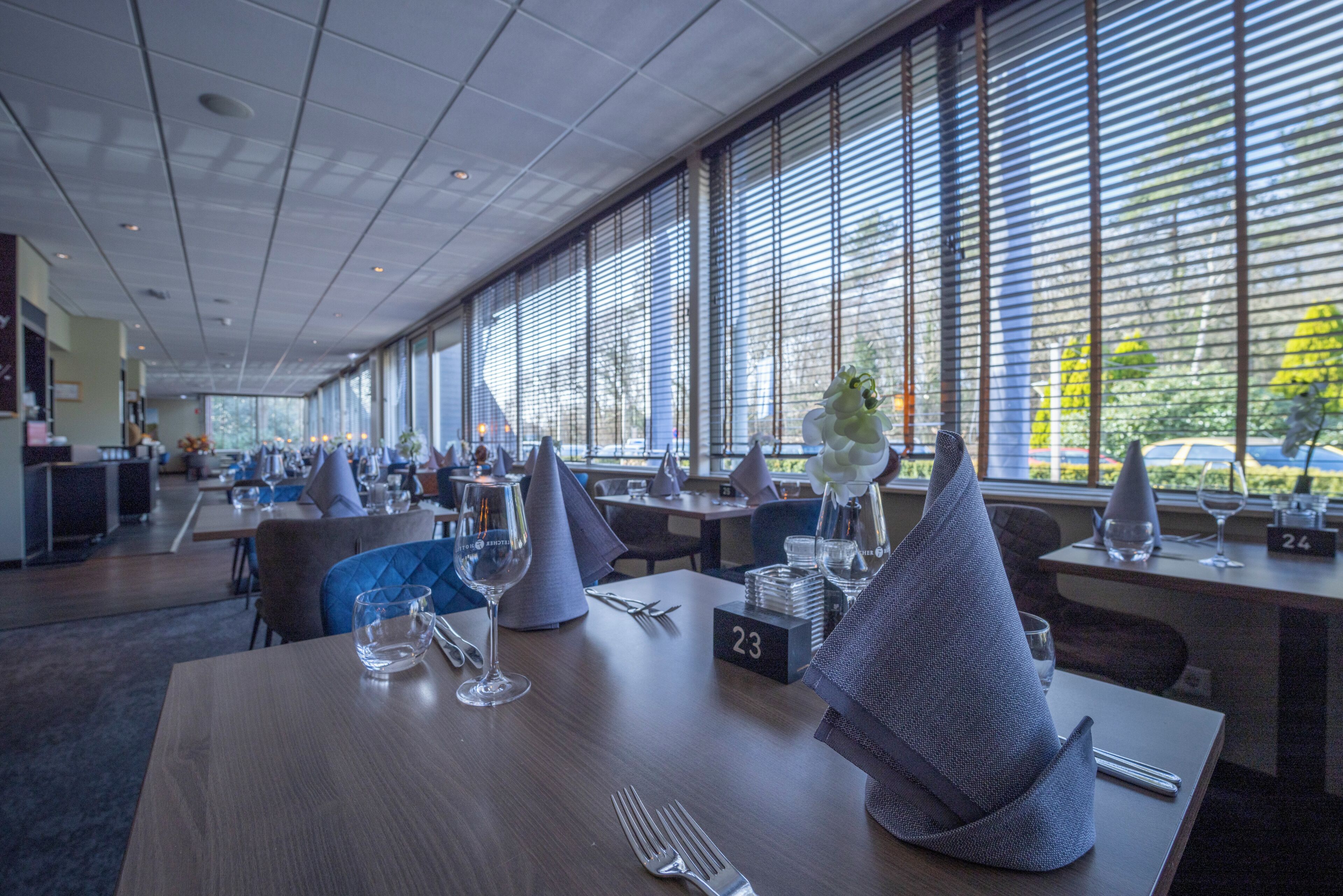 L’intérieur d’un restaurant, avec des tables dressées pour le service, des sets de table numérotés et une vue dégagée grâce à de grandes fenêtres.