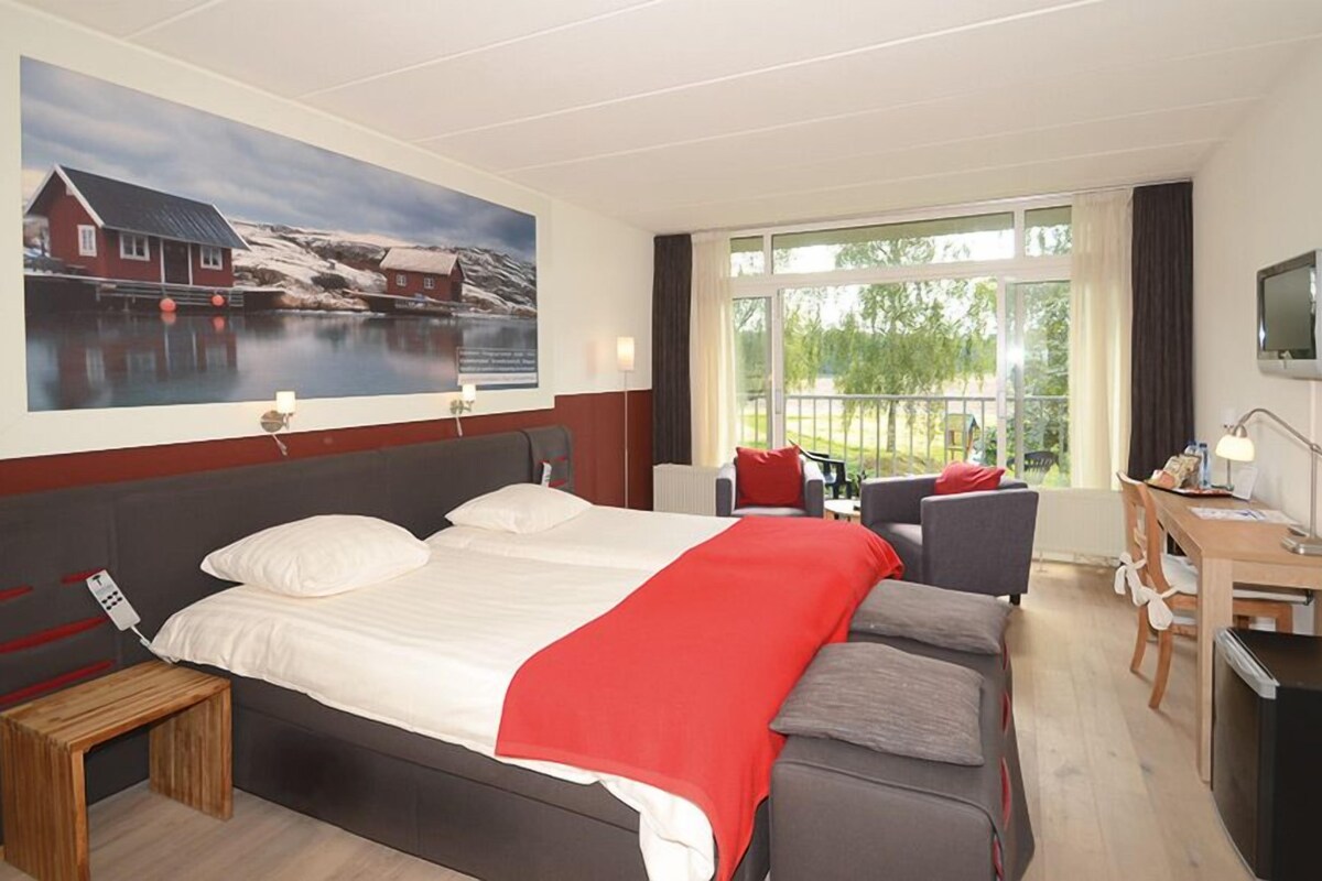 A hotel room with a large bed, a desk, a chair, and a TV.