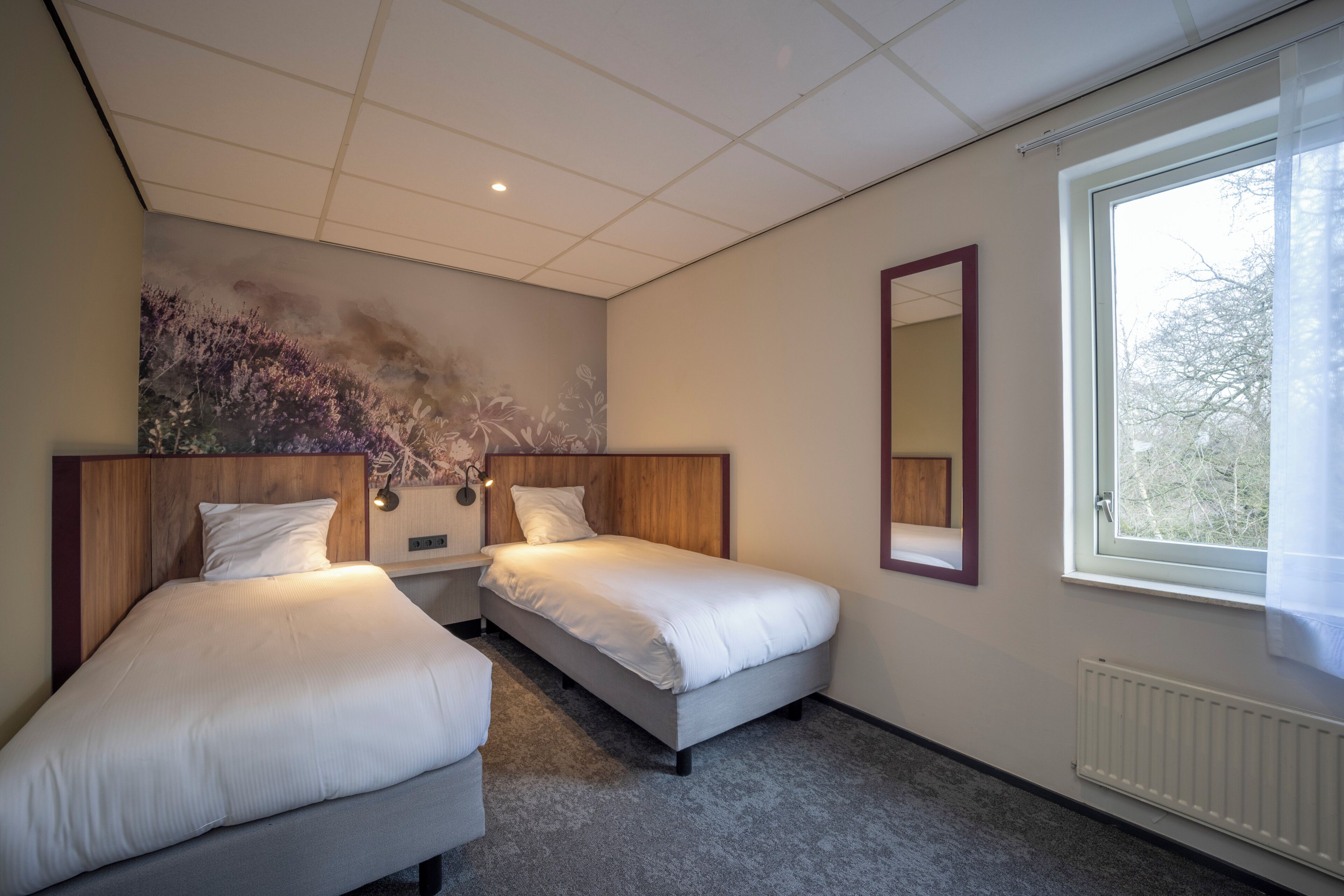 Ein Hotelzimmer mit zwei Betten, einem großen Fenster, einer Heizung und einem Wandbild.