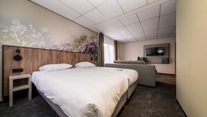 Une chambre d’hôtel avec un grand lit, une petite table, un canapé, une télévision et une fresque murale.
