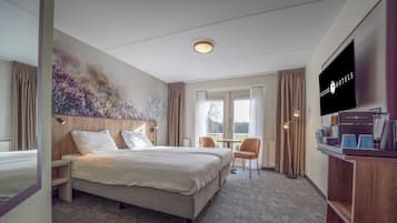 A hotel room with a bed, a desk, a chair, a television, and a window with curtains.
