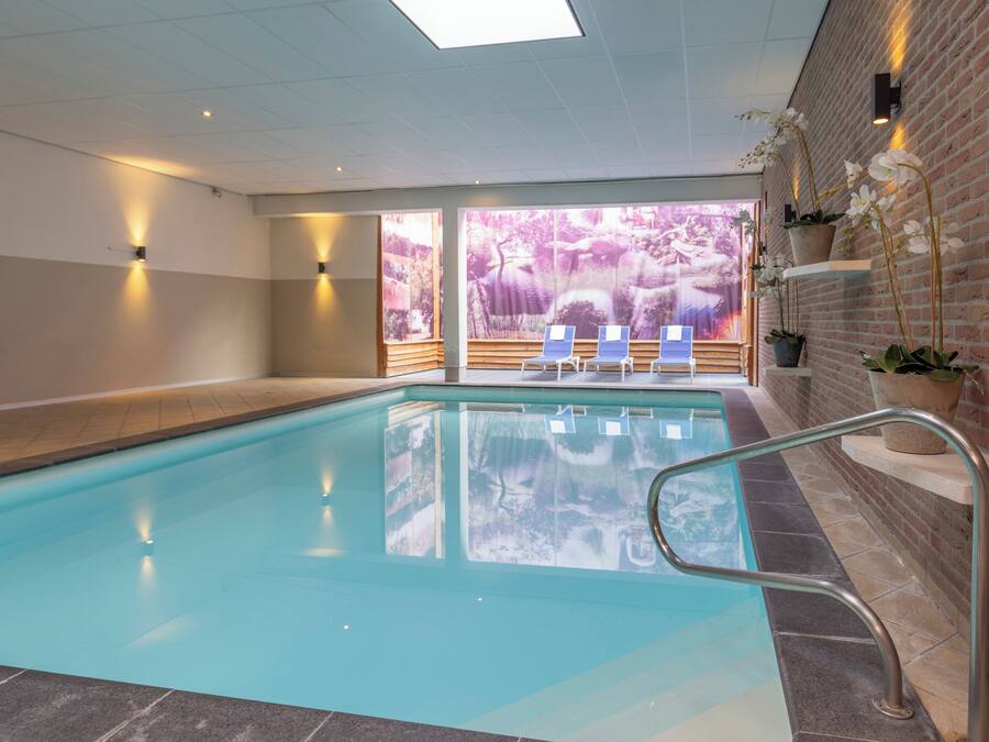 Una piscina interior con paredes de vidrio transparente, una pared de ladrillo en un lado y vistas a un bosque a través del vidrio.