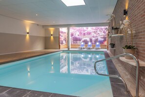 An indoor swimming pool with clear glass walls, a brick wall on one side, and a view of a forest through the glass. - Fletcher Hotel - Restaurant De Zeegser Duinen (Zeegse)