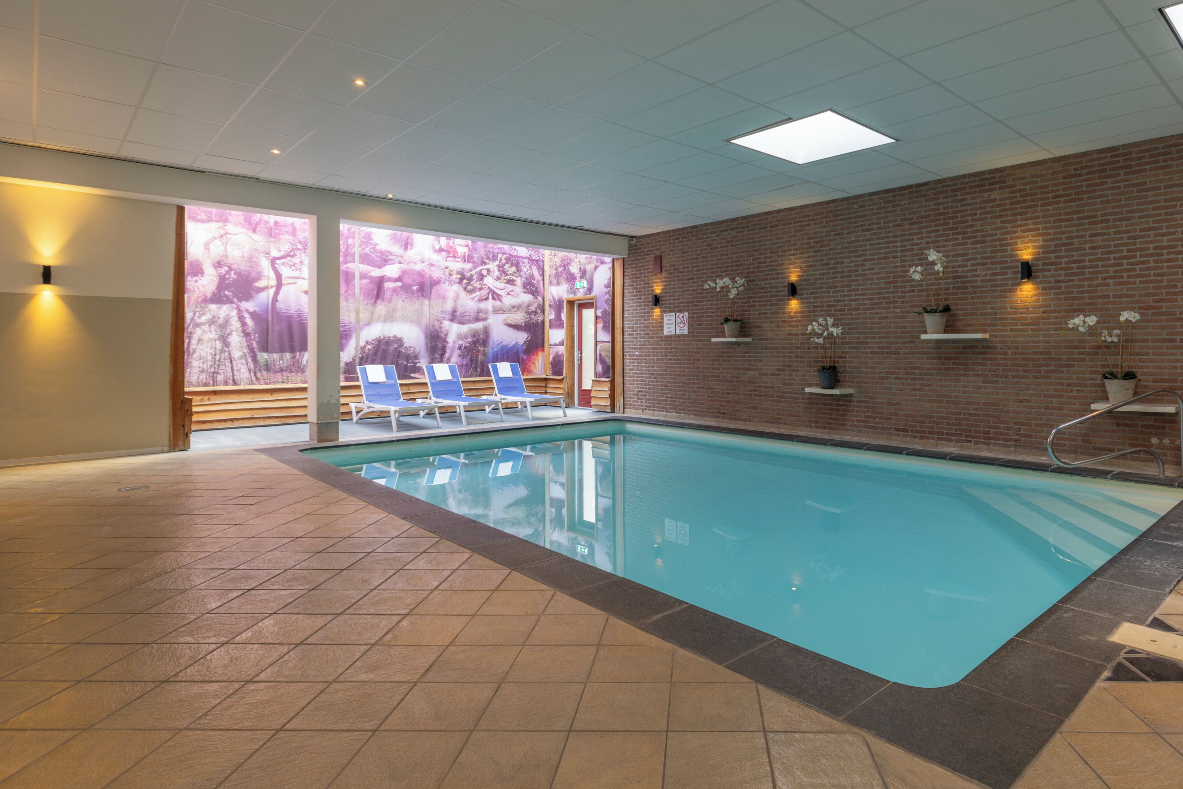 An indoor swimming pool with tiled flooring, blue pool area, and lounge chairs.