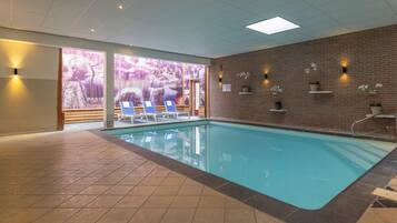 An indoor swimming pool with tiled flooring, blue pool area, and lounge chairs.