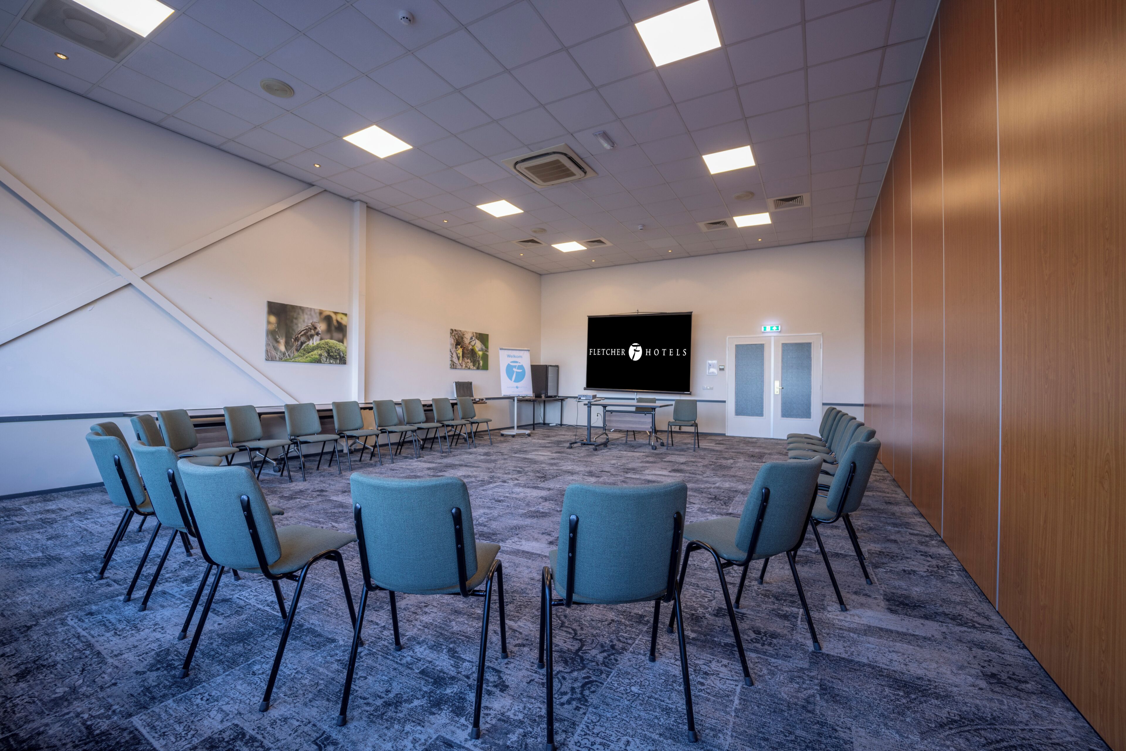 Un salón de conferencias con una pantalla grande, varias filas de sillas y piso alfombrado.
