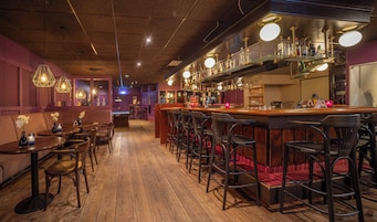 Un área de bar con piso de madera, taburetes y lámparas colgantes.