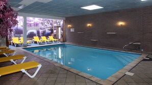 Une piscine intérieure avec des chaises longues jaunes et un mur en briques.