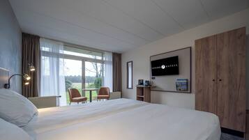 Habitación de hotel con una cama grande, un escritorio con una silla, televisión y una ventana con cortinas.