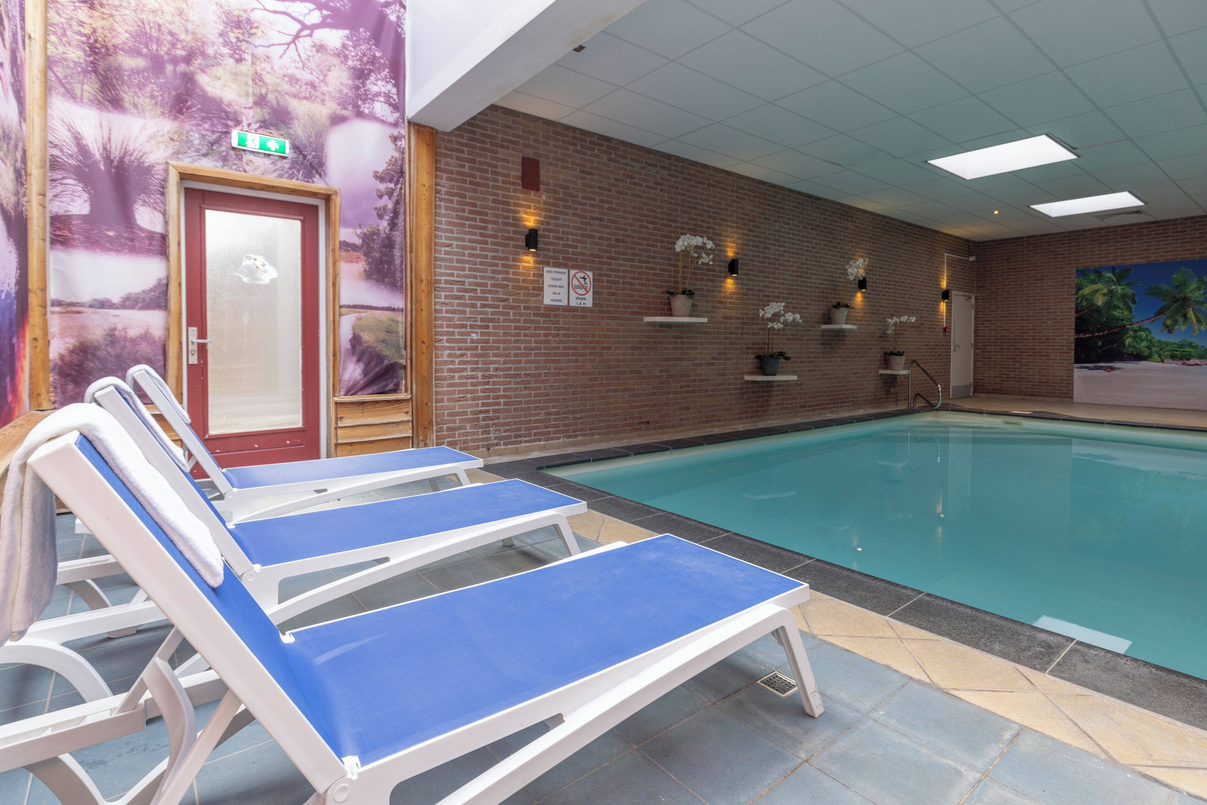 Un espace piscine comprenant des chaises longues, une porte et un mur en briques agrémenté de luminaires et de panneaux indicateurs.