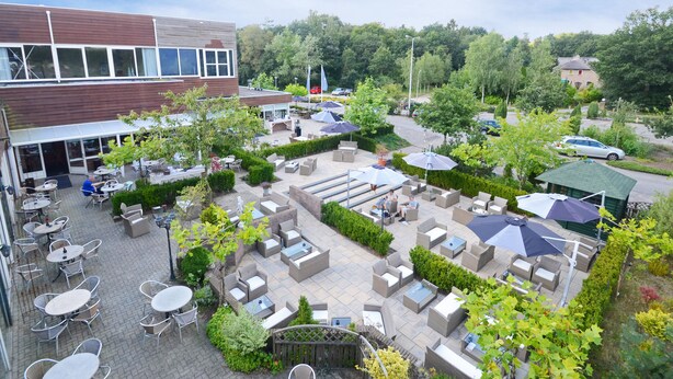 Un espace extérieur aménagé en terrasse, doté de plusieurs coins salon, notamment des tables et des chaises, et entouré de verdure et de parasols.