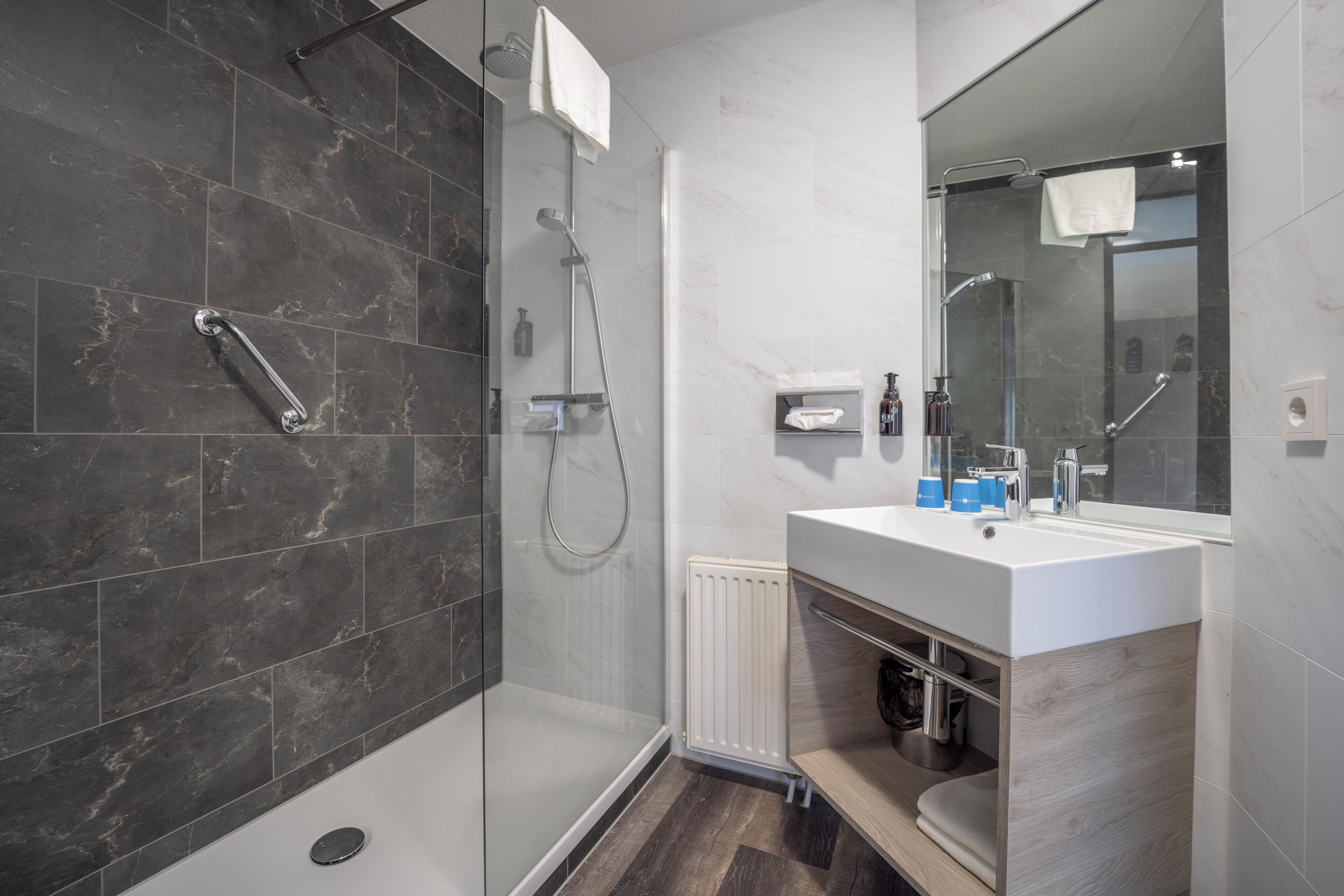 A modern bathroom with a glass-enclosed shower, a white sink with a mirror, and a towel rack.