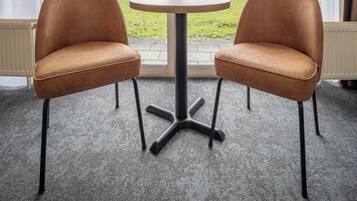 Una habitación con dos sillones de cuero, una mesita redonda y un gran ventanal con cortinas.