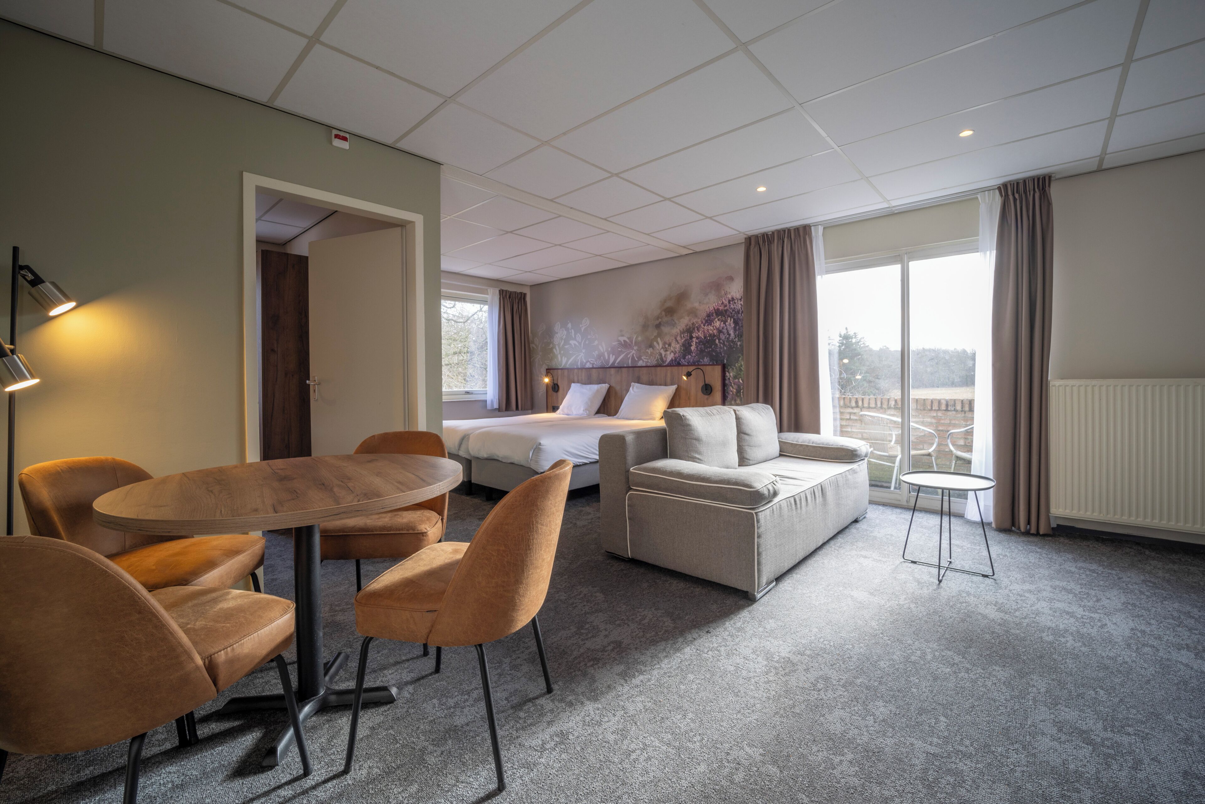 Een hotelkamer met een bed, een bank, een eettafel met stoelen en een klein balkon.