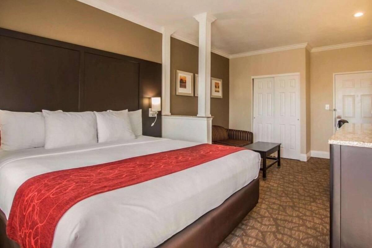 A hotel room with a large bed, a desk, a chair, and two doors.