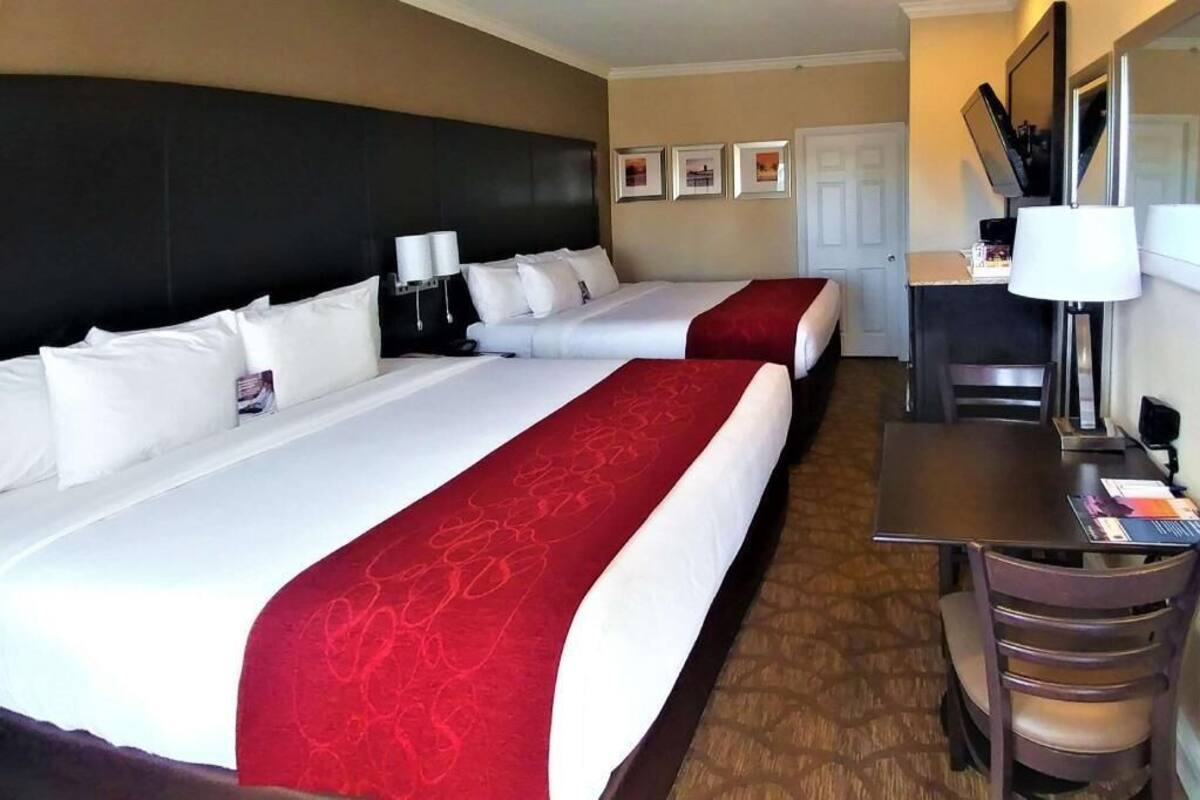 A hotel room with two beds, a desk, a chair, a TV, and a door.