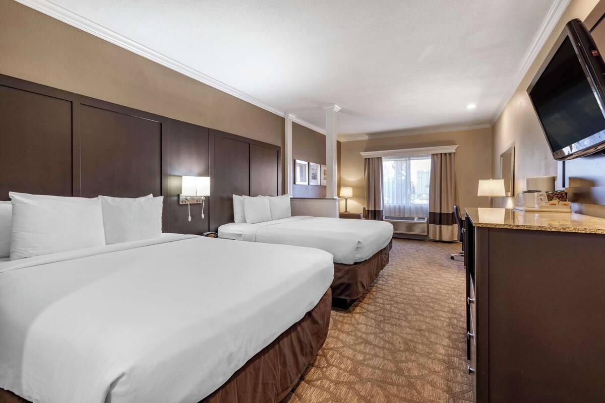 A hotel room with two beds, a desk, a television, and a window with curtains.