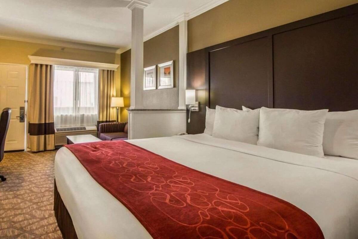A hotel room with a large bed, a desk, a chair, and a window with curtains.