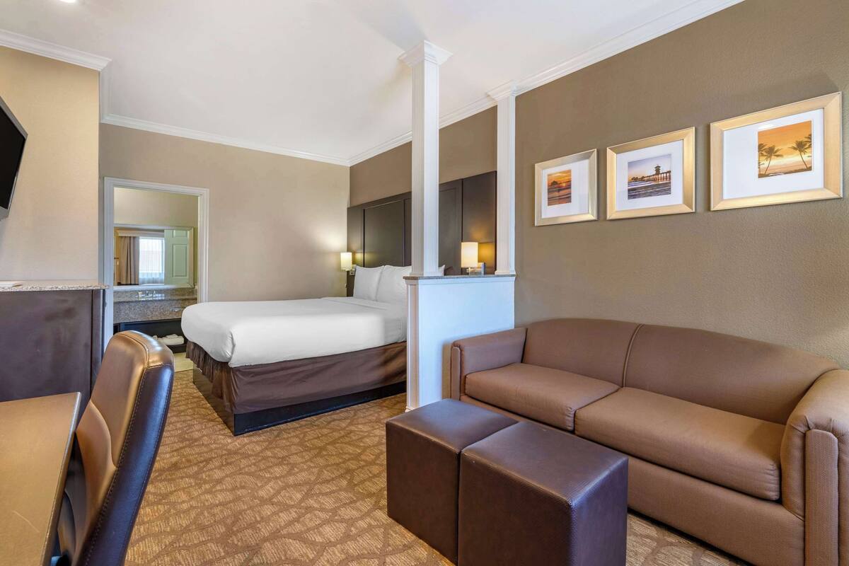 A hotel room with a bed, a sofa, a desk, and a mirror. There are framed pictures on the wall.