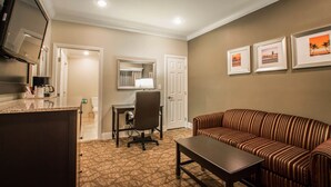 Une chambre d’hôtel équipée d’une kitchenette, d’un canapé, d’un bureau avec une chaise, d’une télévision et de tableaux encadrés au mur.