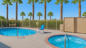 Un espace piscine comprenant deux piscines rondes, des palmiers et un espace délimité par une clôture, avec une chaise et un petit bâtiment.