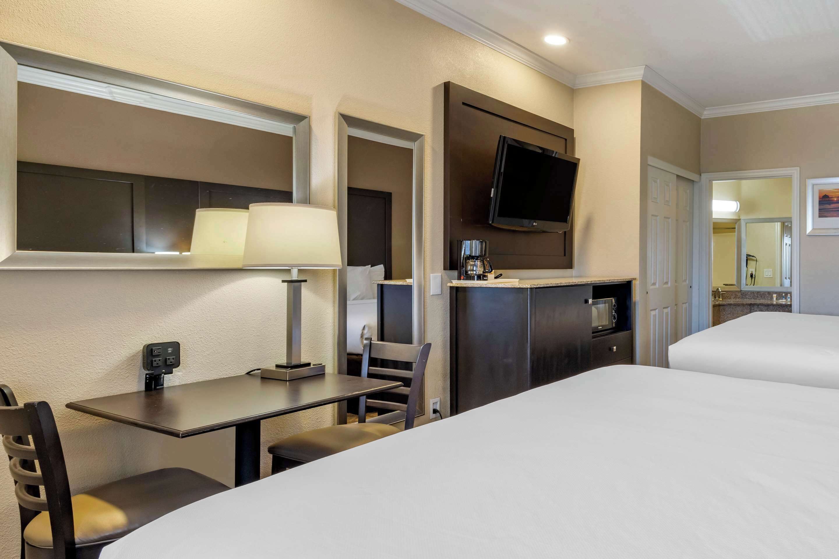 A hotel room with a bed, a desk with a chair, a television mounted on the wall, and a coffee machine.