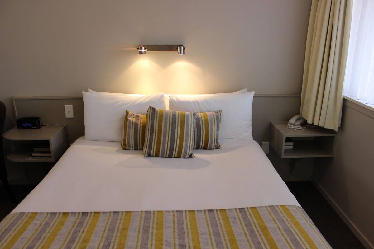 Een hotelkamer met een bed, twee nachtkastjes, een telefoon en een wekker.
