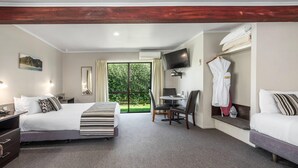 A hotel room with a large bed, a desk, a chair, a TV, and a view of greenery through the window. - Quality Inn Acapulco Taupo (Taupo)