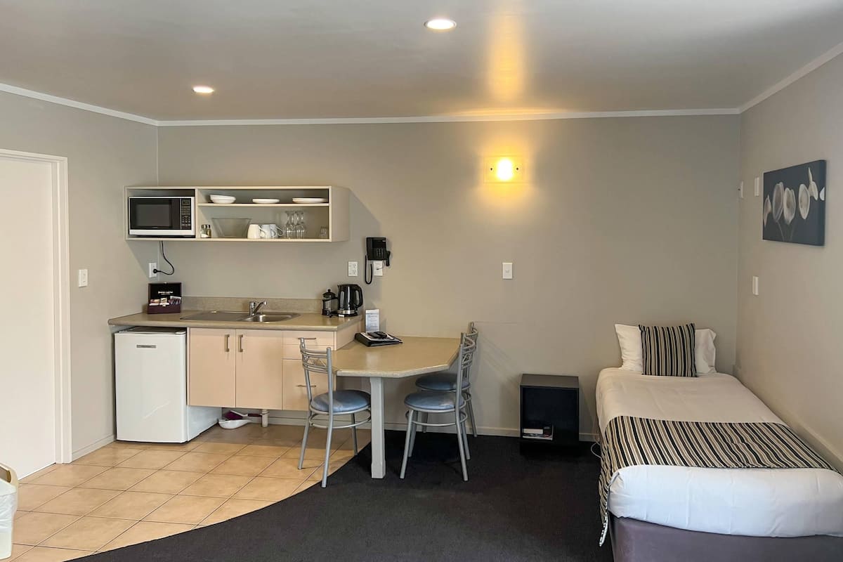 Een kleine kamer met een kitchenette, een bed en een bureau met stoelen.