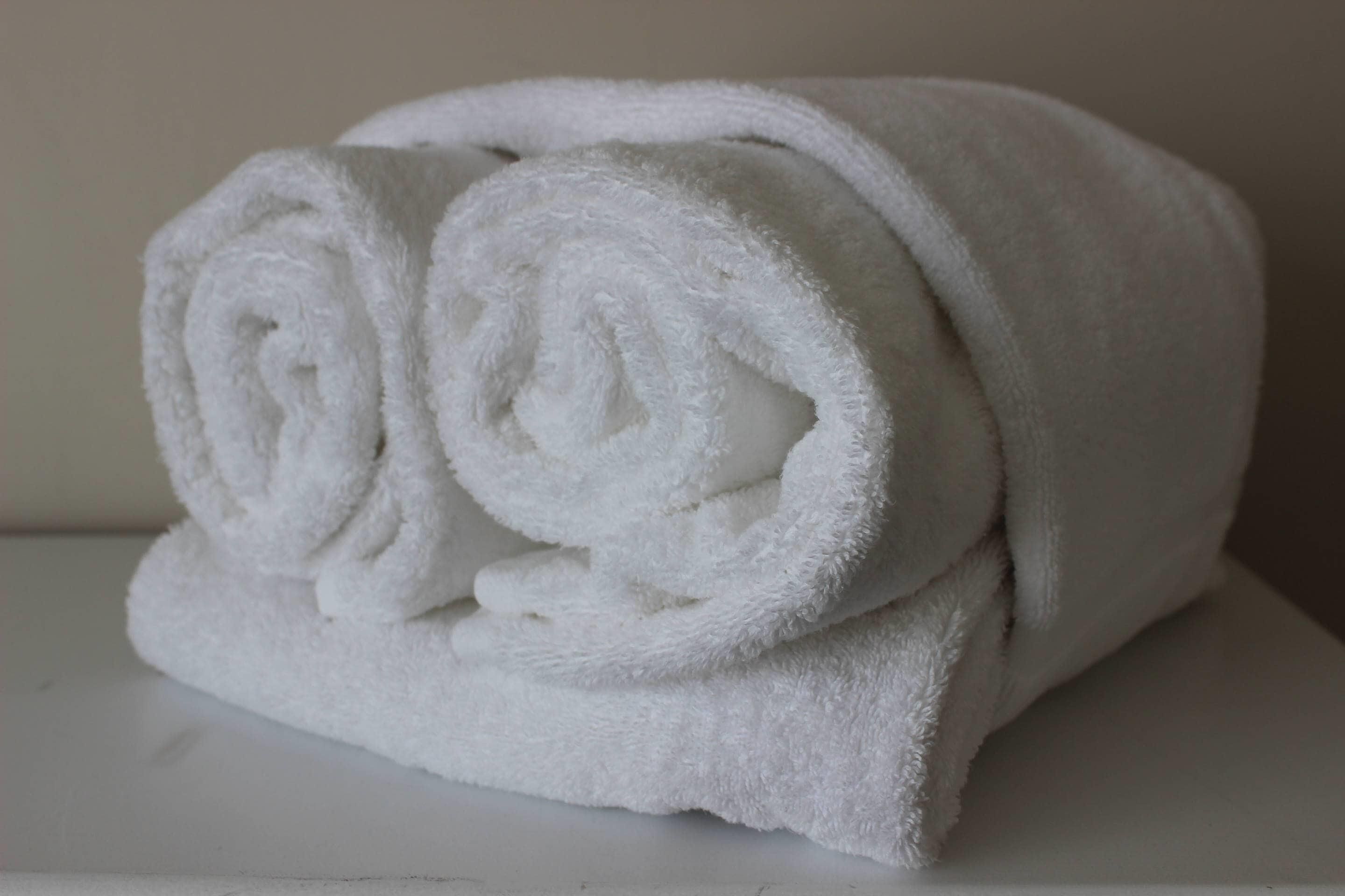 A neatly rolled white towel on a white surface.