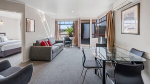 A modern hotel room with a bed, sofa, dining table, chairs, and a balcony with a view. - Quality Inn Acapulco Taupo (Taupo)