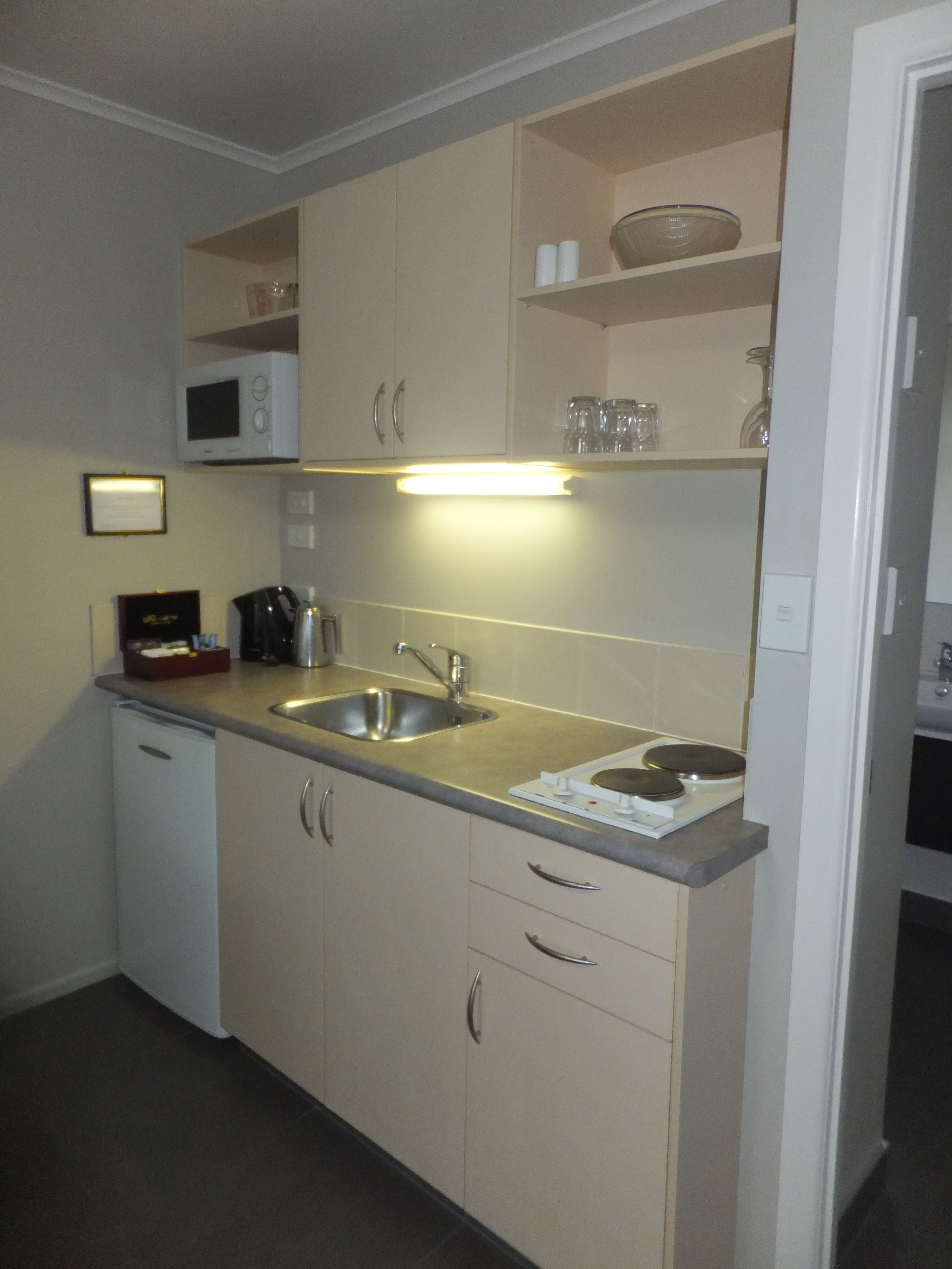 Cocina compacta con microondas, pileta y cocina. Hay alacenas y una mesada.