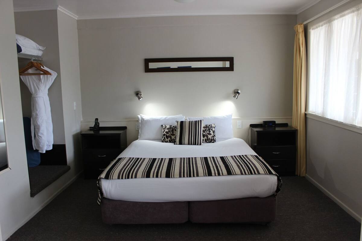 Een hotelkamer met een groot bed, twee nachtkastjes, een spiegel en een garderobe.