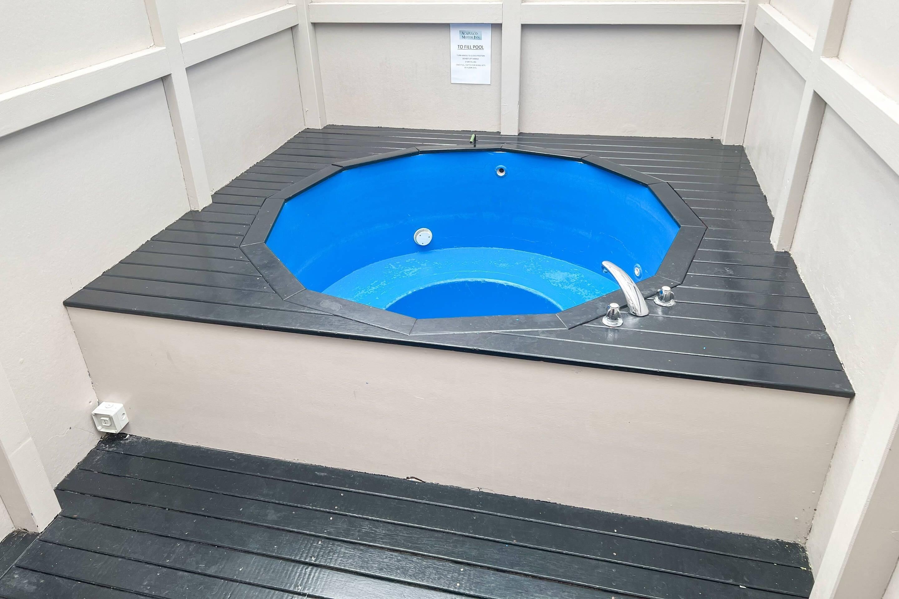 A hot tub with a black rim and a blue interior, surrounded by beige walls and a black floor.