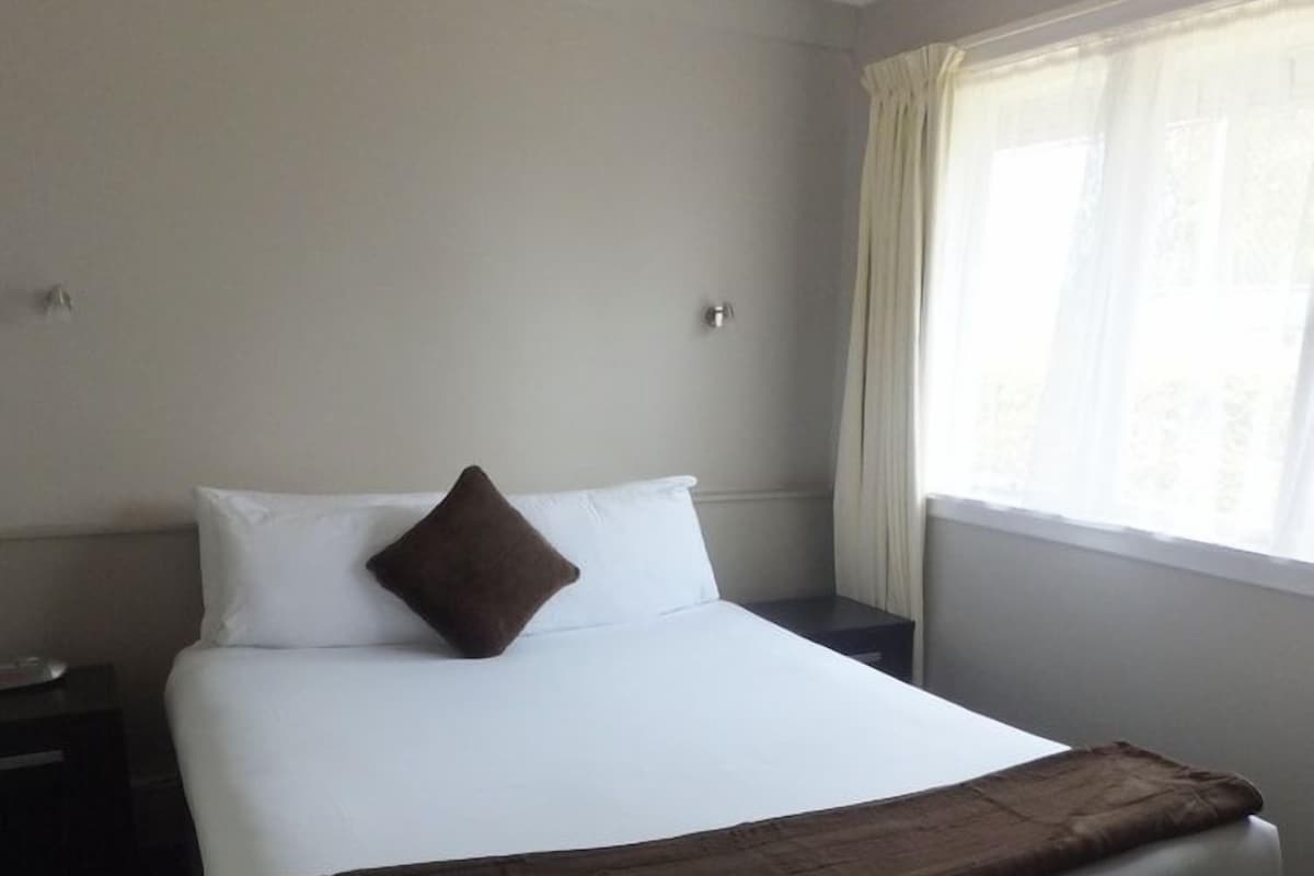 A hotel room with a large bed, a nightstand, and a window with curtains.