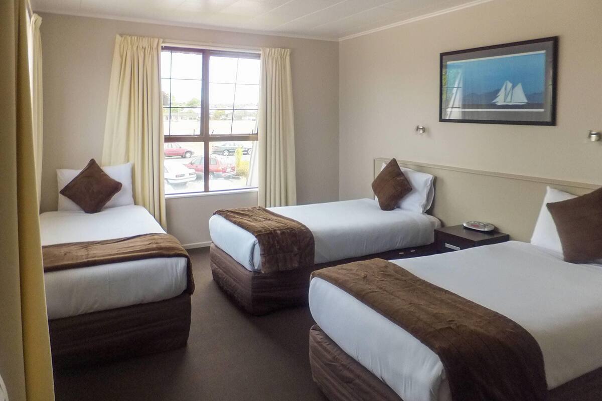 Hotelkamer met drie eenpersoonsbedden, een raam met gordijnen, een schilderij aan de muur en uitzicht op de omgeving.