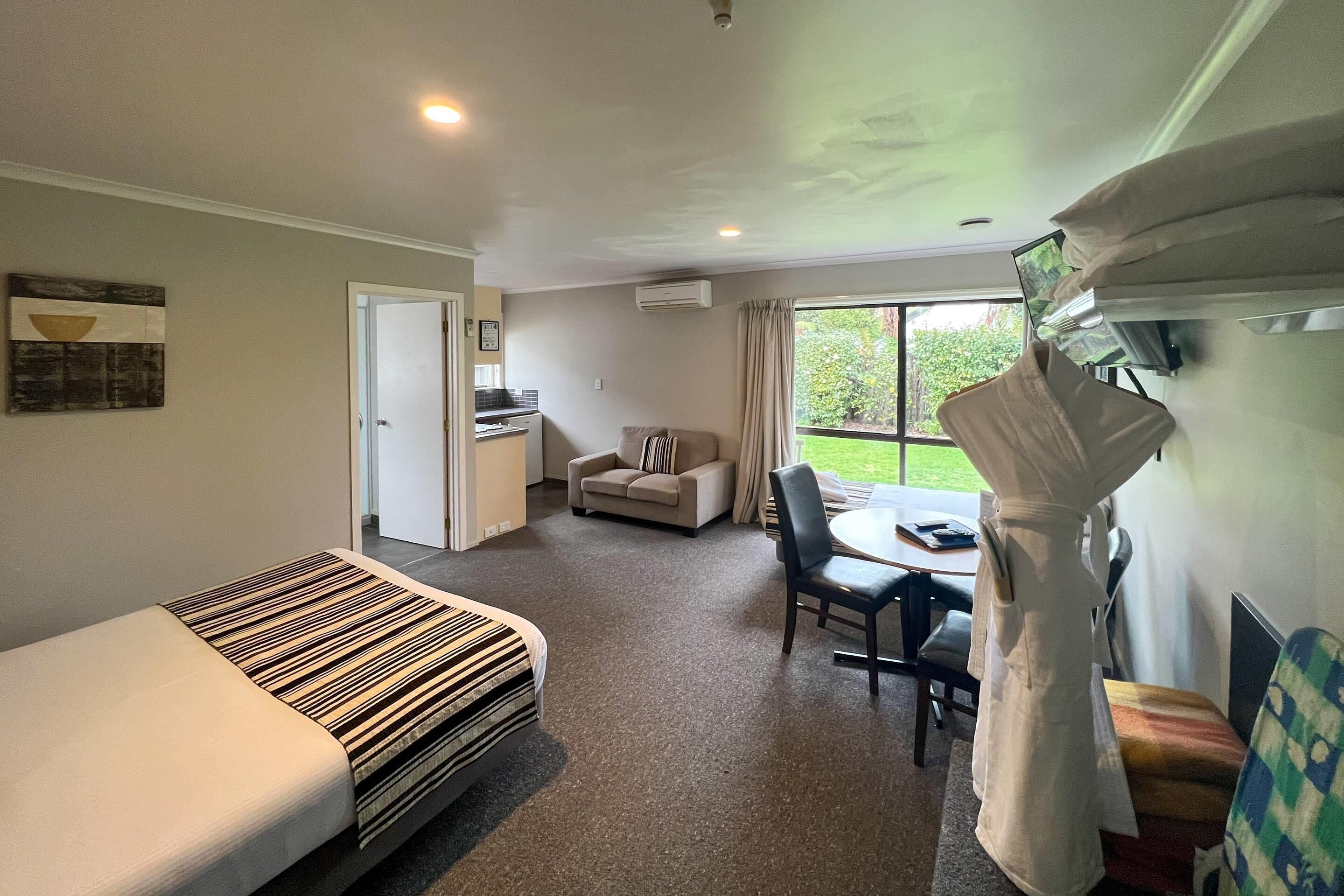 A hotel room with a bed, a sofa, a dining table, and a view of the outdoors.