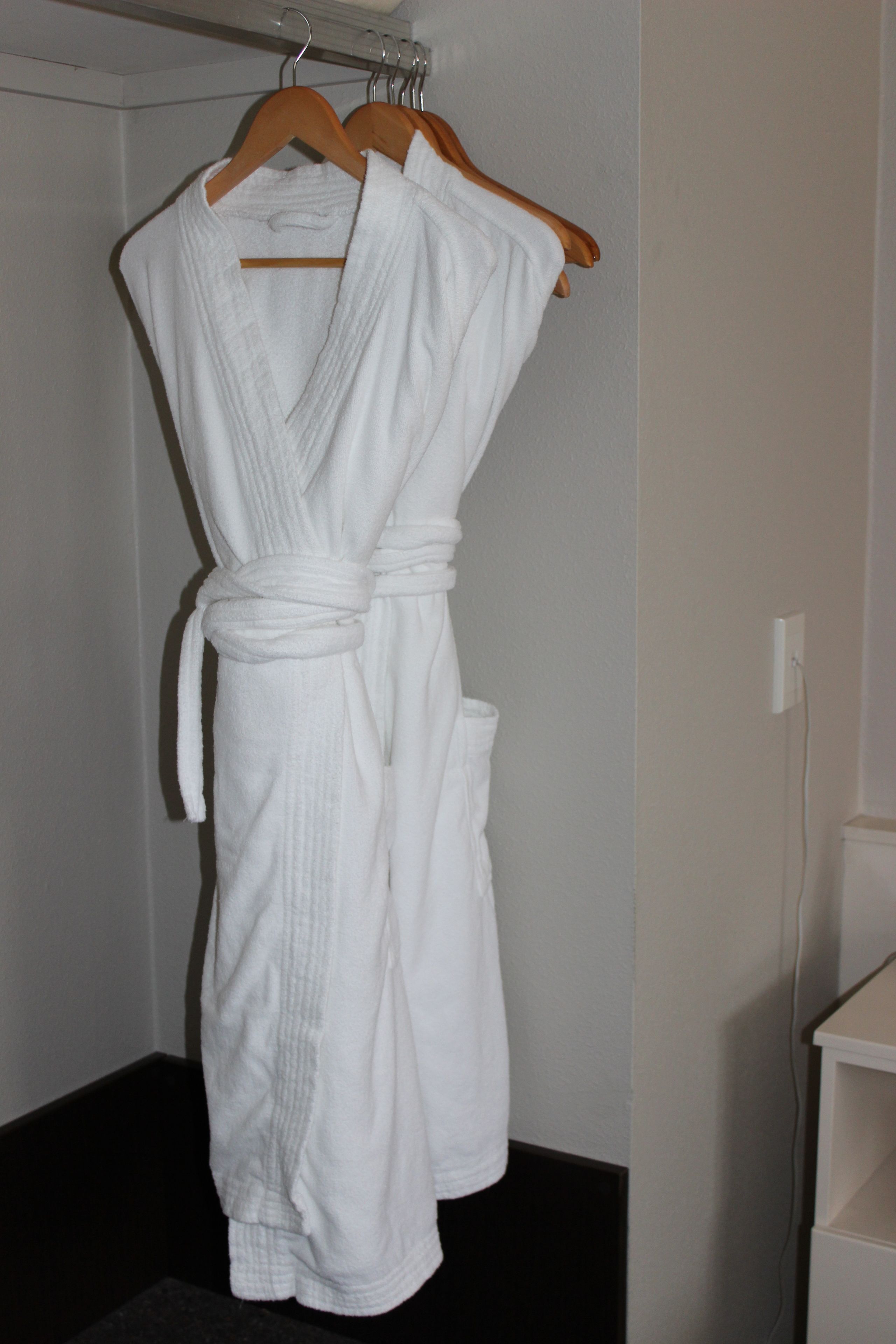 A white bathrobe hanging on a wooden hanger in a bathroom.