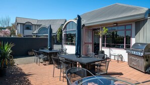 An outdoor patio with tables and chairs, a grill, and a building with large windows and a sign. - Quality Inn Acapulco Taupo (Taupo)