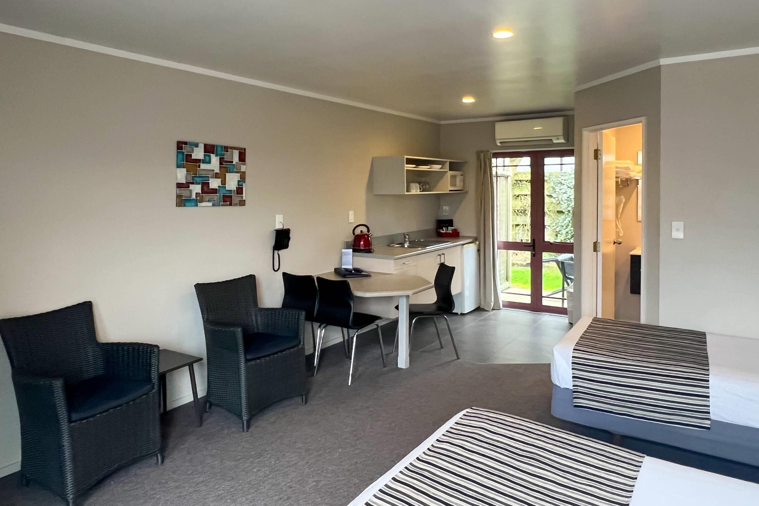 A compact hotel room with a kitchenette, a dining area with two chairs, a bed, and a view of the outdoors.