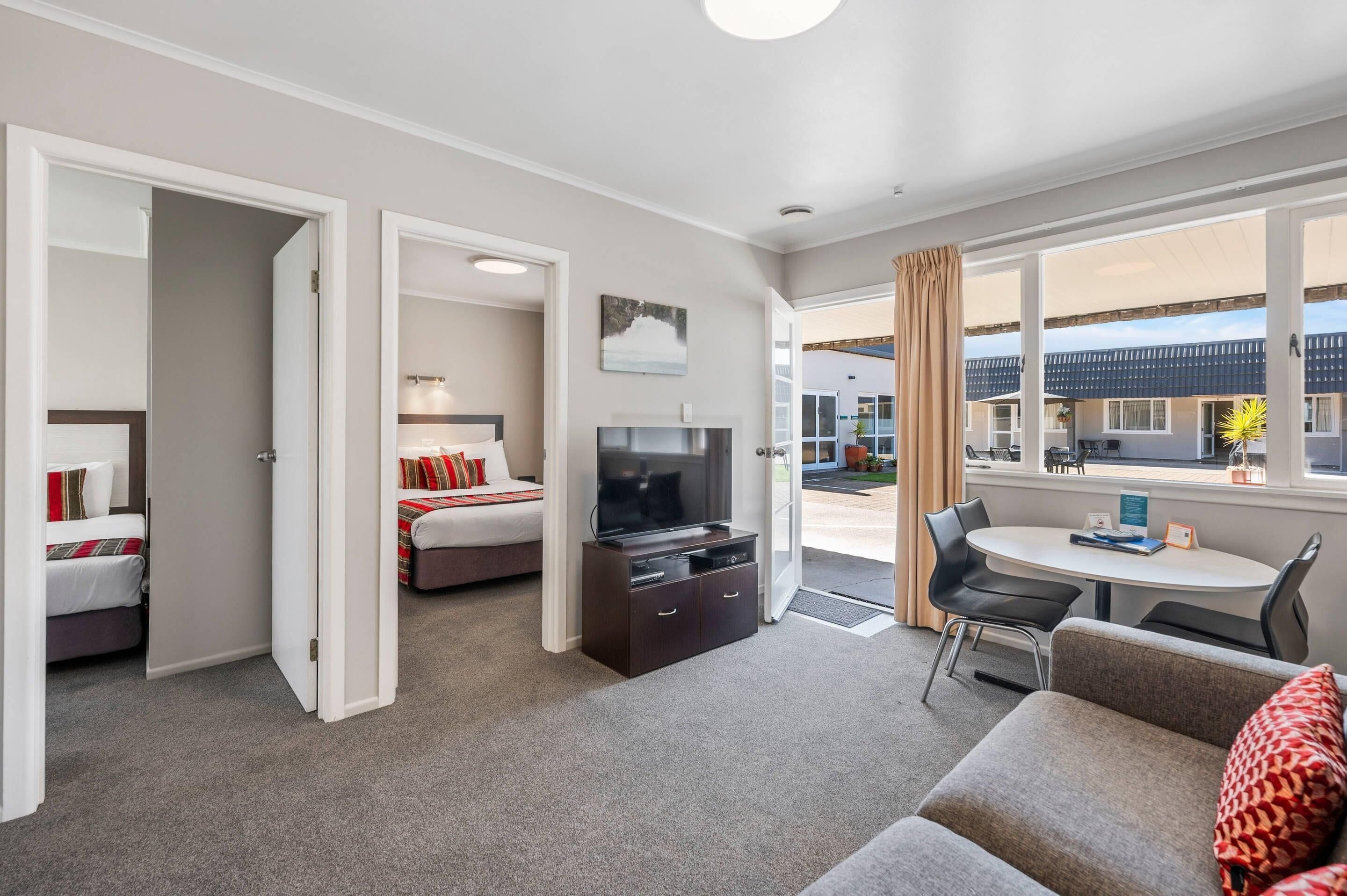 A modern hotel room with a sofa, a TV, a dining table, and a view of the outside.