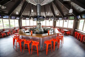 A bar area with a central counter, multiple screens, and red chairs. - Hampton Inn Frederick (Frederick)
