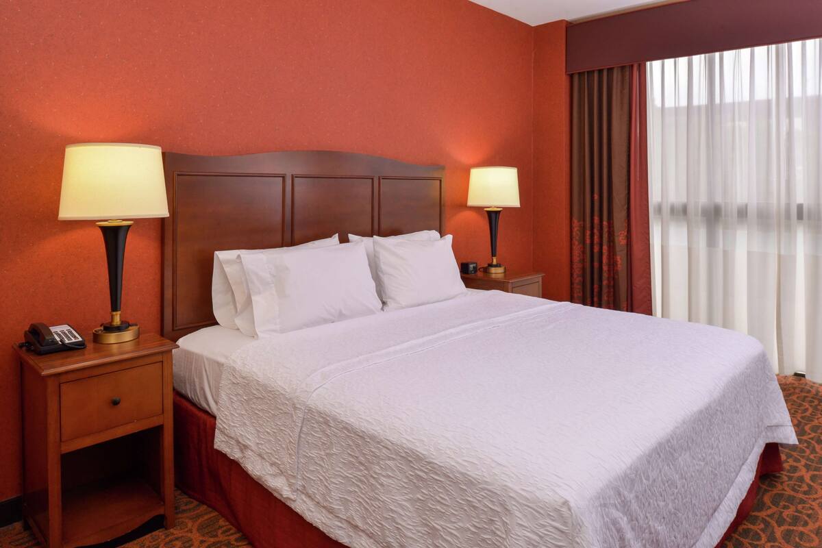 A hotel room with a large bed, two bedside lamps, a nightstand with a phone, and a window with curtains.