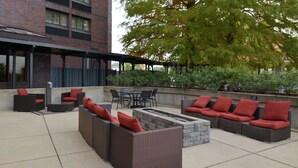 Eine Terrasse im Freien mit Korbmöbeln, roten Kissen und einem Steinkamin.