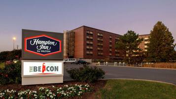 Une enseigne Hampton Inn by Hilton avec le logo distinctif de la chaîne, entourée de fleurs et d’un parking.