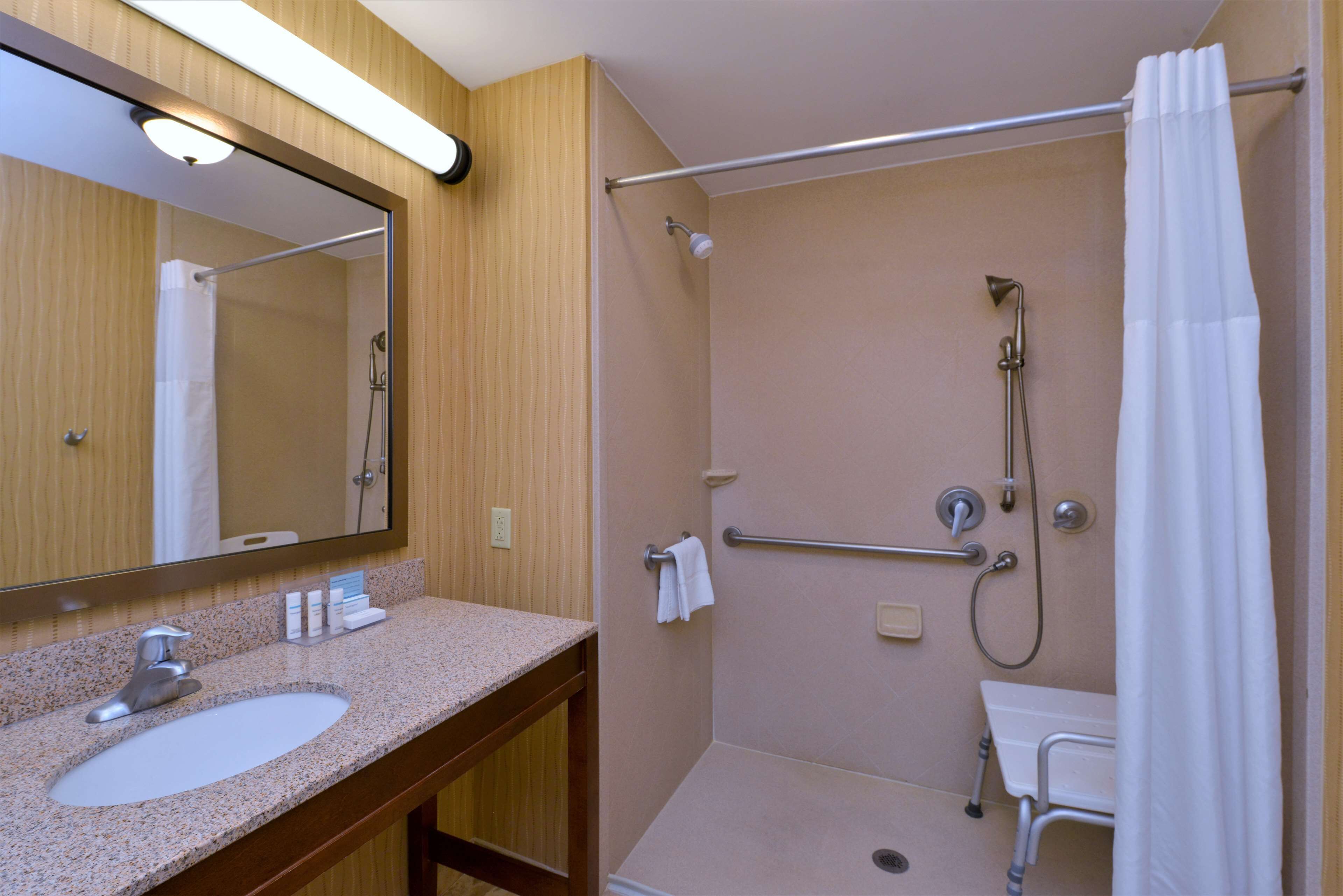 A bathroom with a sink, mirror, shower, and grab bar.
